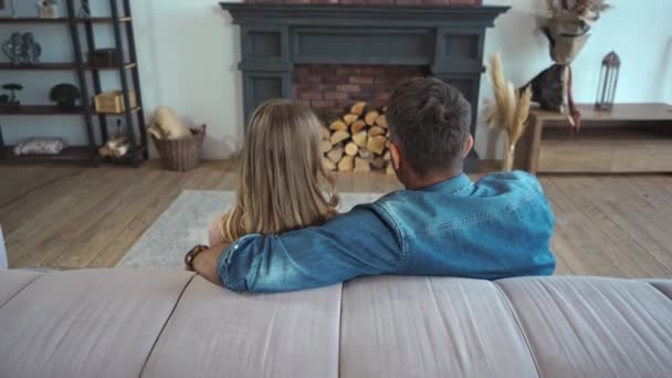 Πίσω όψη ζευγαριού που μιλάει και αγκαλιάζεται στον καναπέ στο σπίτι - Πλάνα, βίντεο