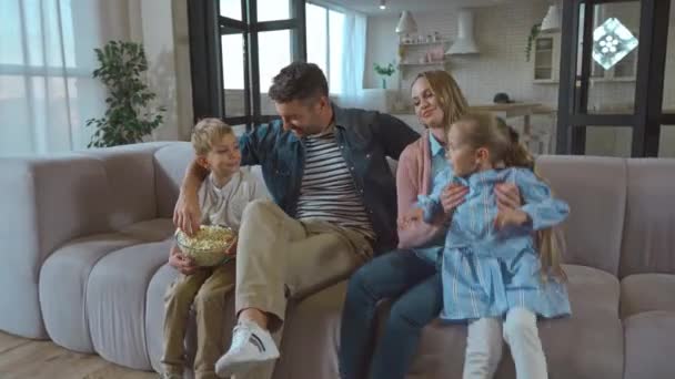 陽気な両親と子供が話している間に食べるポップコーンオンソファに家 - 映像、動画