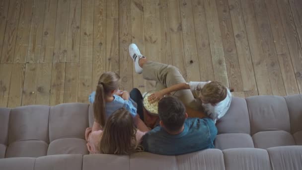 Vista dall'alto della famiglia che mangia popcorn mentre è seduta sul divano a casa - Filmati, video