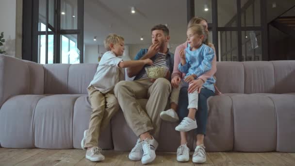 Volledige lengte van glimlachende familie met popcorn praten terwijl het kijken van tv thuis - Video