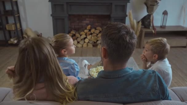 Zadní pohled na rodiče s dětmi jíst popcorn na gauči v obývacím pokoji - Záběry, video