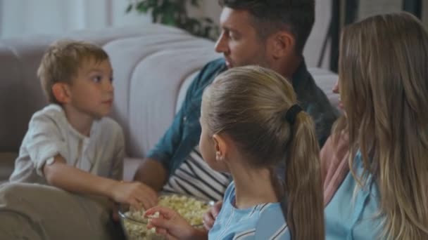 Sonriente familia hablando con su hijo comiendo palomitas en el sofá en la sala de estar - Imágenes, Vídeo