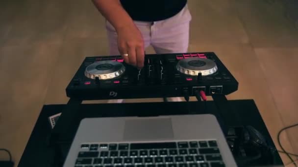 Caucasian DJ with wedding ring on hand stands behind laptop and music mixer and creates cool dance atmosphere and use lighting effects for people who want to relax and have fun in evening at disco  - Footage, Video