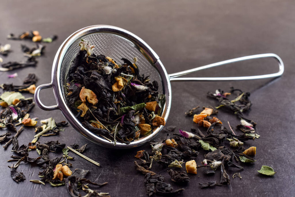 Metalen, aluminium infusiefilter gevuld met droge thee gemaakt van fruit en kruiden en bloemen, zwarte achtergrond. Gezonde en smakelijke thee. - Foto, afbeelding