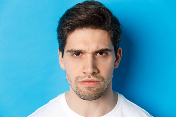 Голова рассерженного человека хмурящегося, выглядящего разочарованным и обеспокоенным, стоящего на синем фоне - Фото, изображение