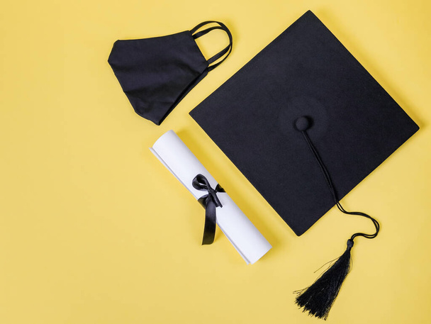 Graduation cap, mask and diploma on the right on a yellow background with space for text on the left, top view close-up. - Photo, Image