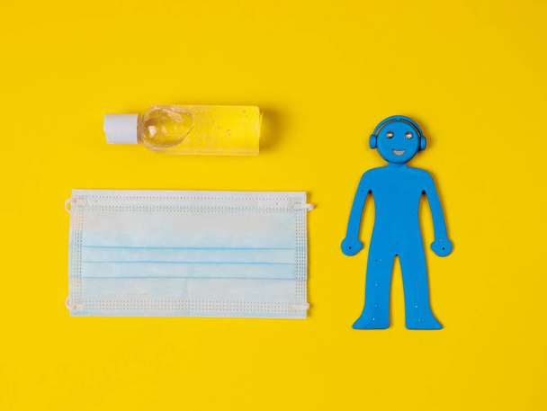 A blue man, a medical mask and a disinfectant lie in the middle on a yellow background, a close-up top view. - Φωτογραφία, εικόνα