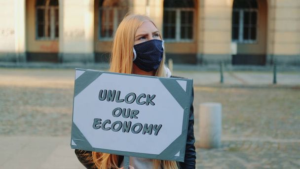 Młoda kobieta w masce medycznej wzywa do odblokowania gospodarki trzymając parowiec - Zdjęcie, obraz