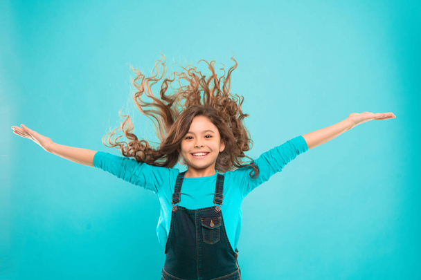 Experiencing a hair to balance your energy. Adorable girl curly hair waving on blue background. Small cute girl with long brunette hair wearing casual style. Little hair model with fashion look - 写真・画像