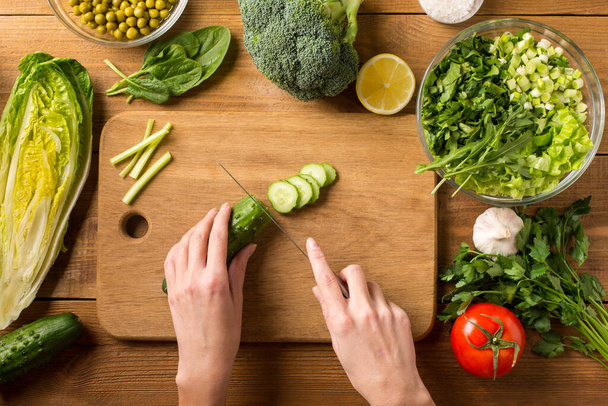 Preparare un'insalata di verdure fresche. Taglio di cetriolo fresco su un tagliere. Mani femminili. - Foto, immagini