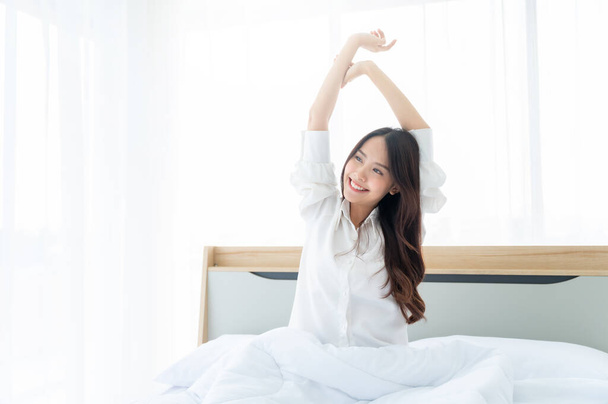 Kauniit naiset aasialainen herätä aamulla makuuhuoneessa. Hän on venyttely ja tunne tuoretta - Valokuva, kuva