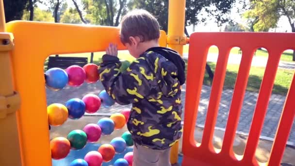 Lassan mozgó felvétel egy kisfiúról, amint abakáló gömbökkel játszik egy parkban..  - Felvétel, videó