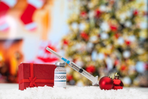 Butelka szczepionki, strzykawka, czerwone pudełko i czerwone kulki świąteczne stoją w śniegu na tle choinki - Zdjęcie, obraz