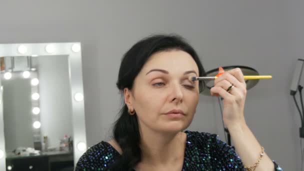 Mladá krásná showy žena v přední části zrcadla aplikuje tvář a oční make-up se speciálním štětcem - Záběry, video