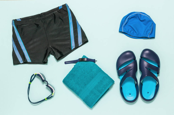 Malles de natation, ardoises, lunettes de natation et une serviette sur fond bleu. Pose plate. - Photo, image
