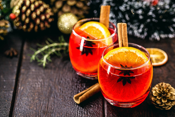 Mulled red wine with spices and Christmas fruits on a rustic wooden table with Christmas colors and lights. Traditional hot drink at Christmas time - Фото, зображення