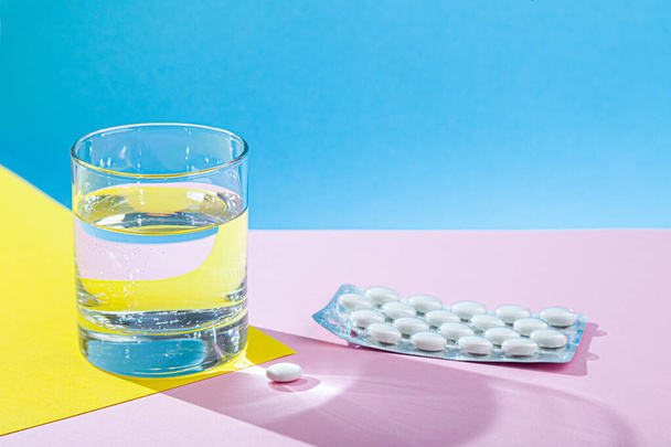 Vizespohár, orvosi tablettákkal, tablettákkal, vitaminokkal ellátott buborékcsomagolás rózsaszín alapon - Fotó, kép