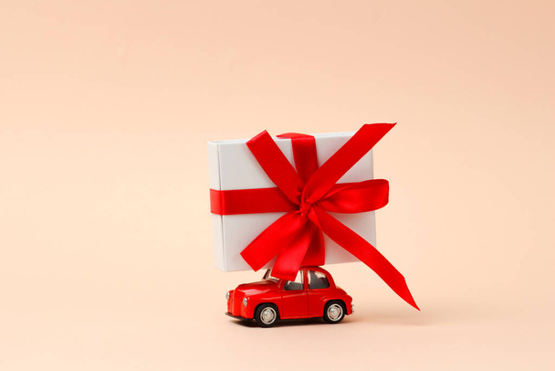  Small red retro toy car with a big gift on the roof on a pink background. Delivery of gifts for Christmas, Valentine's Day, World Women's Day. Sale concept. - Foto, imagen