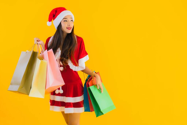 Portrait beautiful young asian woman wear christmas clothes hat with a lot of shopping bag on yellow isolated background - Fotó, kép