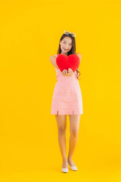 Portrait beautiful young asian woman with heart pillow sign on yellow isolated background - Foto, Imagen
