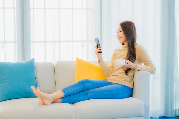 Portrait beautiful young asian woman with smart mobile phone on sofa in living room interior - Zdjęcie, obraz