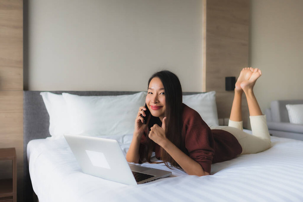 Retrato hermosa joven asiático mujeres utilizando ordenador y teléfono móvil en la cama en el interior del dormitorio - Foto, Imagen
