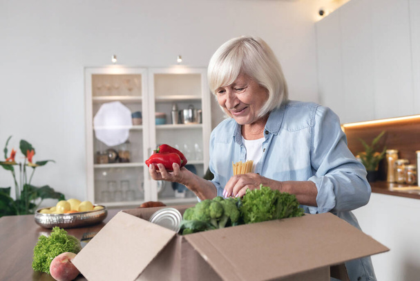 Adult woman unpacks box of groceries that was delivered to her home - 写真・画像