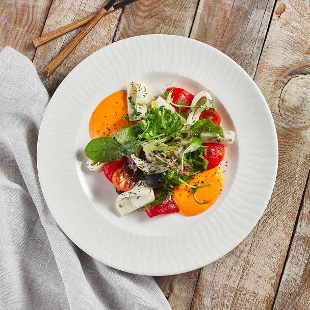 Roasted pepper salad with calamari and fresh greens. Rustic wooden table and grey textile - Foto, Imagem