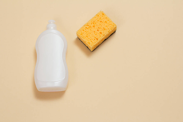 Bottiglia di plastica di liquido per piatti e una spugna sullo sfondo beige. Vista dall'alto. Set di lavaggio e pulizia. - Foto, immagini