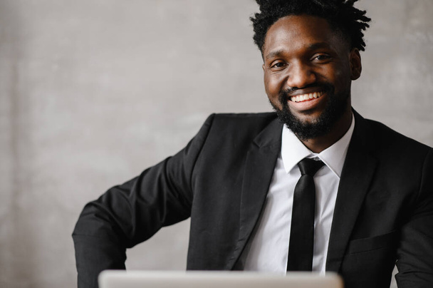  Handsome african american businessman in classic suit uses laptop and smiles while working in office - Fotografie, Obrázek
