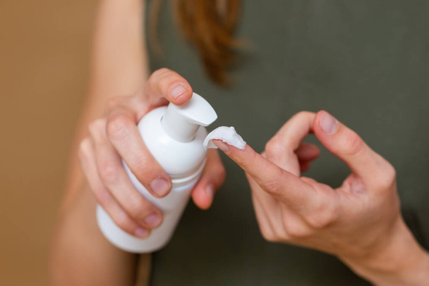 jonge vrouw persen een container van crème aan de vinger - Foto, afbeelding