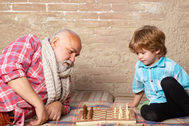 Küçük çocuk büyükbabasıyla satranç oynuyor. Satranç taşı. Son sınıf öğrencisi satranç oyunundaki bir sonraki hamlesini düşünüyor.. - Fotoğraf, Görsel