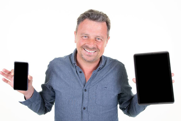 человек стоит планшет и смартфон обеих рук держа черный мобильный телефон с черным пустым экраном - Фото, изображение
