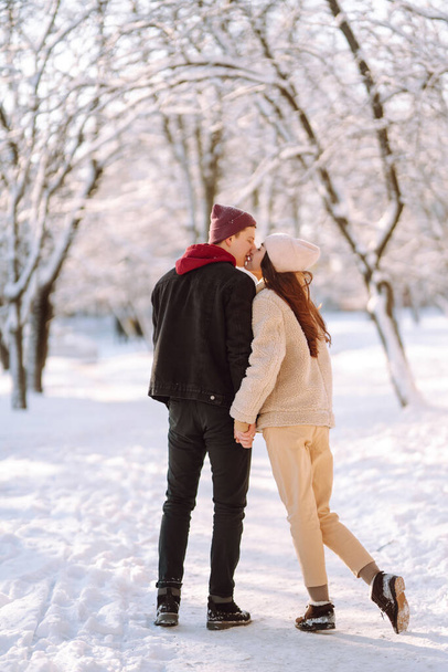 Happy couple hugging and kissing outdoors in winter park. Young man and woman enjoy each other in snow forest. Holidays, season, love and leisure concept. - Foto, Imagem