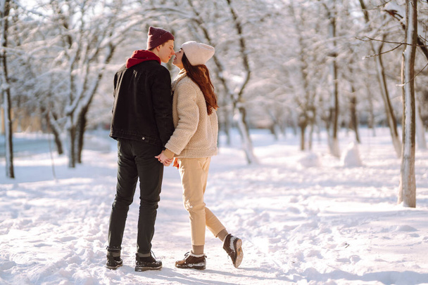 Happy couple hugging and kissing outdoors in winter park. Young man and woman enjoy each other in snow forest. Holidays, season, love and leisure concept. - Fotó, kép