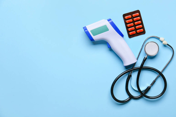 Infrared thermometer, stethoscope and pills on color background - Photo, Image