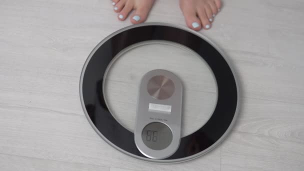 a női lábak elektromos mérlegen és az eredményjelző táblán 76,6 kg-os súllyal helyezkednek el. - Felvétel, videó