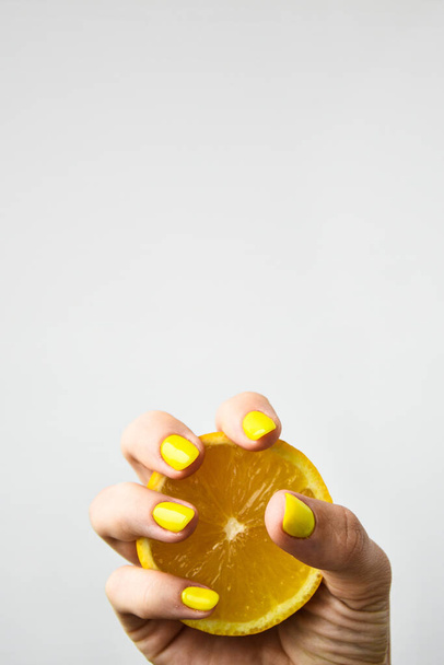 Weibliche Hand mit stylischen gelben Nägeln, die frische Zitrone halten. Weibliche Maniküre. glamourös schöne Maniküre. Kopierraum. - Foto, Bild