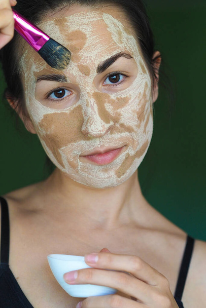 junge brünette Frau mit einer hausgemachten Maske aus Ton auf dem Gesicht - Foto, Bild
