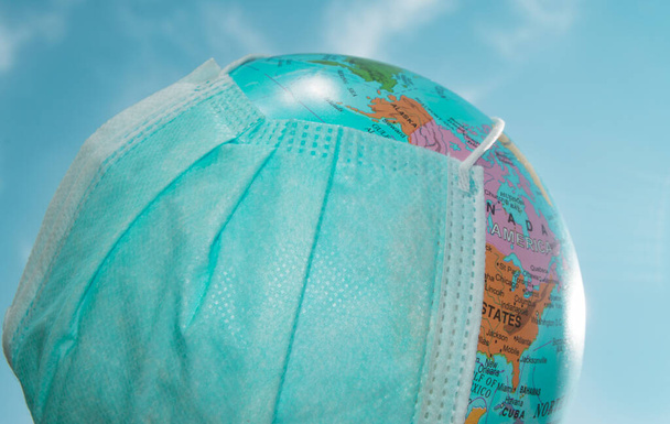 A globe in a medical mask against a blue sky. A worldwide pandemic, the concept of protection against coronavirus, outdoor, summer. - Fotografie, Obrázek