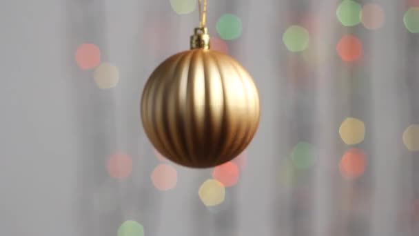 Gyönyörű karácsonyfa játék lóg a háttérben a sokszínű újévi fények. Közelkép. Karácsonyfa játék formájában gömb arany színű. - Felvétel, videó