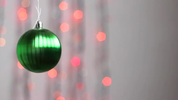 Schöne Weihnachtsbaumspielzeug hängt vor dem Hintergrund der bunten Weihnachtsbeleuchtung und bewegt sich leicht. Nahaufnahme. Weihnachtsbaumspielzeug in Form einer grünen Kugel. - Filmmaterial, Video