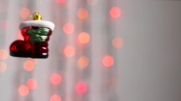 Beautiful Christmas tree toy hangs against the background of multi-colored Christmas lights and moves slightly. Close-up. Christmas tree toy in the form of a red boot.Camera movement panorama - Footage, Video