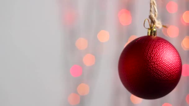 Beautiful Christmas tree toy hangs against the background of multi-colored Christmas lights and moves slightly. Close-up. Christmas tree toy in the form of a red sphere.Camera movement panorama - Footage, Video