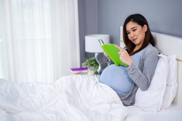 pregnant woman reading a book on a bed - Fotó, kép