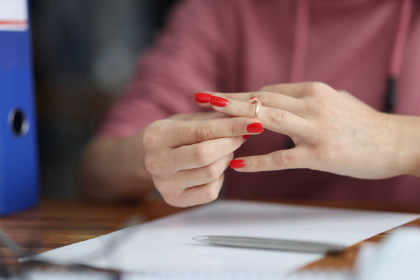 Woman taking off her wedding ring from her finger in front of documents close-up - Fotoğraf, Görsel
