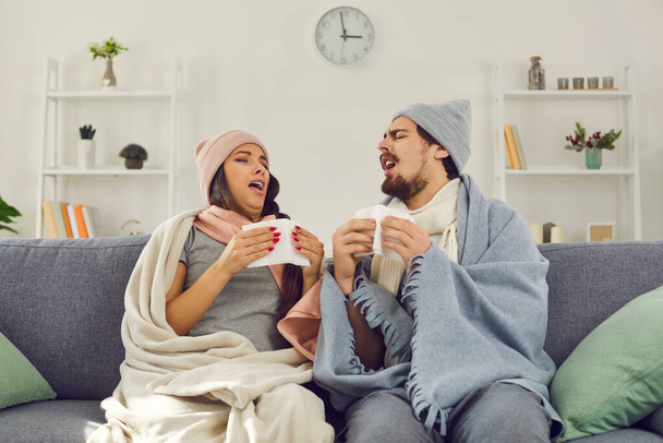 Young couple wrapped in warm blankets sitting on couch and sneezing in paper tissues - Photo, image