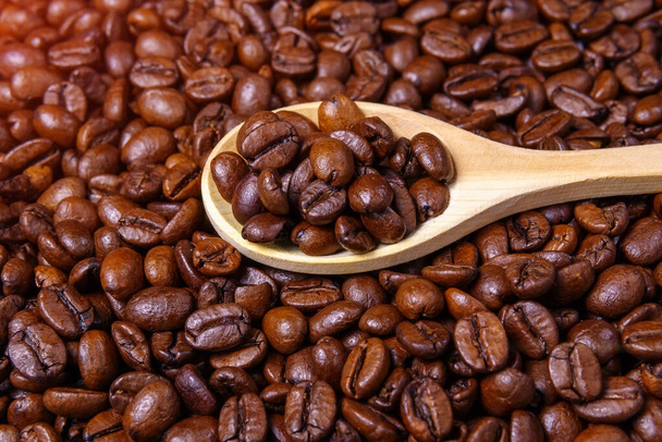 Жареные кофейные зерна крупным планом в деревянной ложке. селективный фокус - Фото, изображение