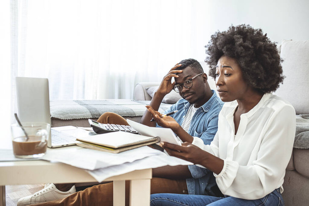 Stressed african american couple looking frustrated, having no money to pay off their debts, managing family budget together, sitting home at kitchen table with lots of papers, laptop and calculator - Valokuva, kuva