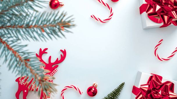 Święta zimowa czerwień. Białe pudełko ze szkarłatną wstążką, piłeczki noworoczne, cukierki i choinka zimowa w kompozycji świątecznej na białym tle dla kartki okolicznościowej. Ozdoba świąteczna, przestrzeń do kopiowania - Zdjęcie, obraz